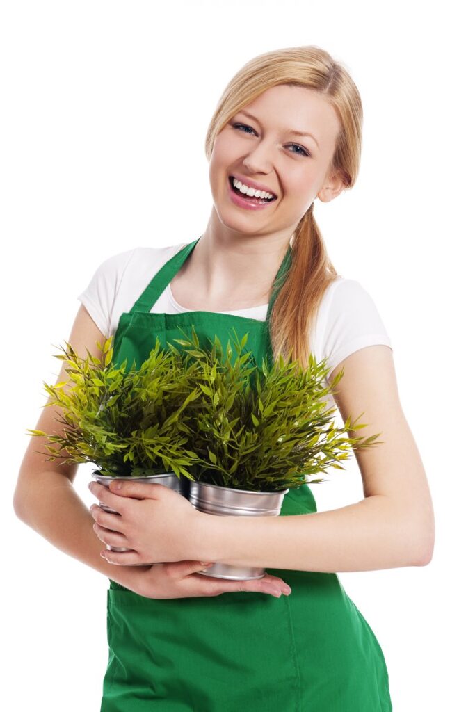 Chica rubia sonriente con vestimenta de jardinera portando varias plantas